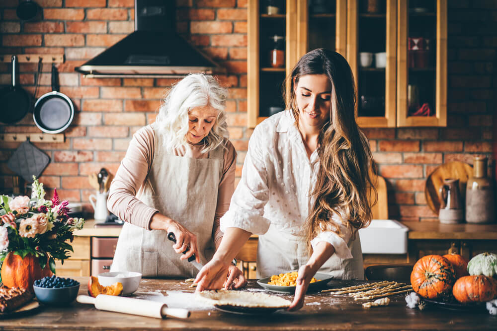 A young woman and her grandmother are baking pumpkin pies in a cozy kitchen